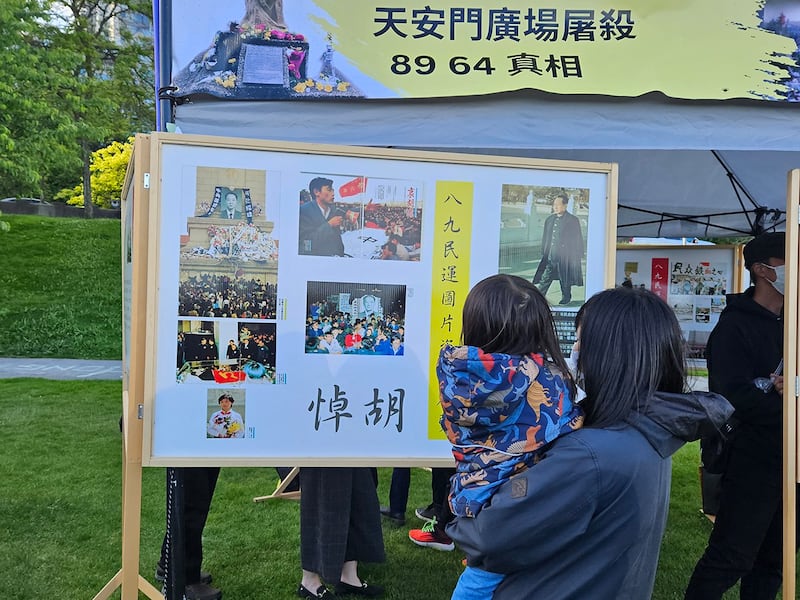 有父母带着年幼孩子来参与活动,在看板前对孩子说明六四的历史,希望播下一粒未来的民主种子。(记者柳飞拍摄)