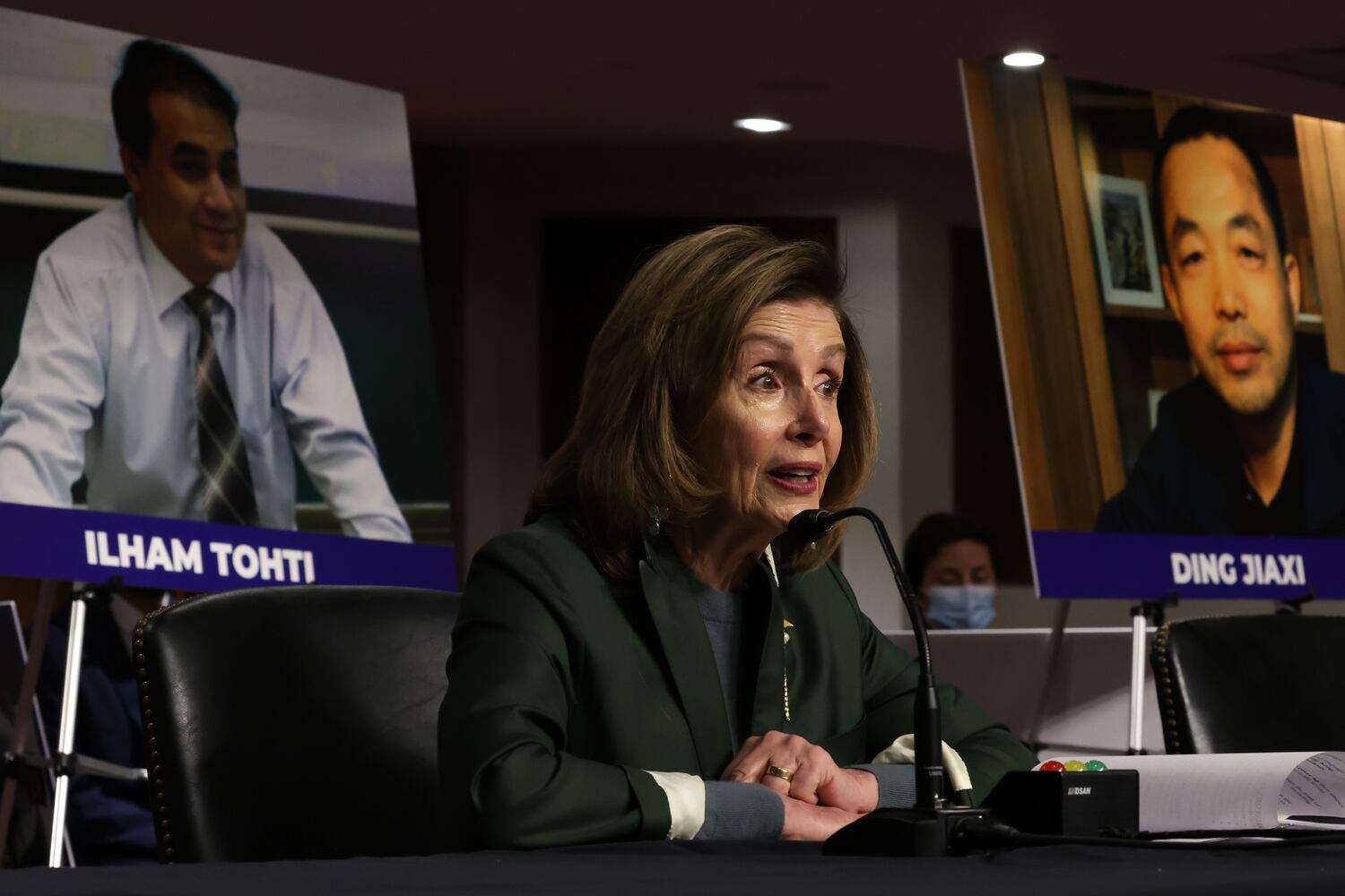 As photos of Uyghur scholar Ilham Tohti, left, and Chinese human rights activist Ding Jiaxi, right,  are seen in the background, U.S. Speaker of the House Rep. Nancy Pelosi speaks during a hearing before The Congressional-Executive Commission on China (CECC)  Feb. 3, 2022 in Washington.