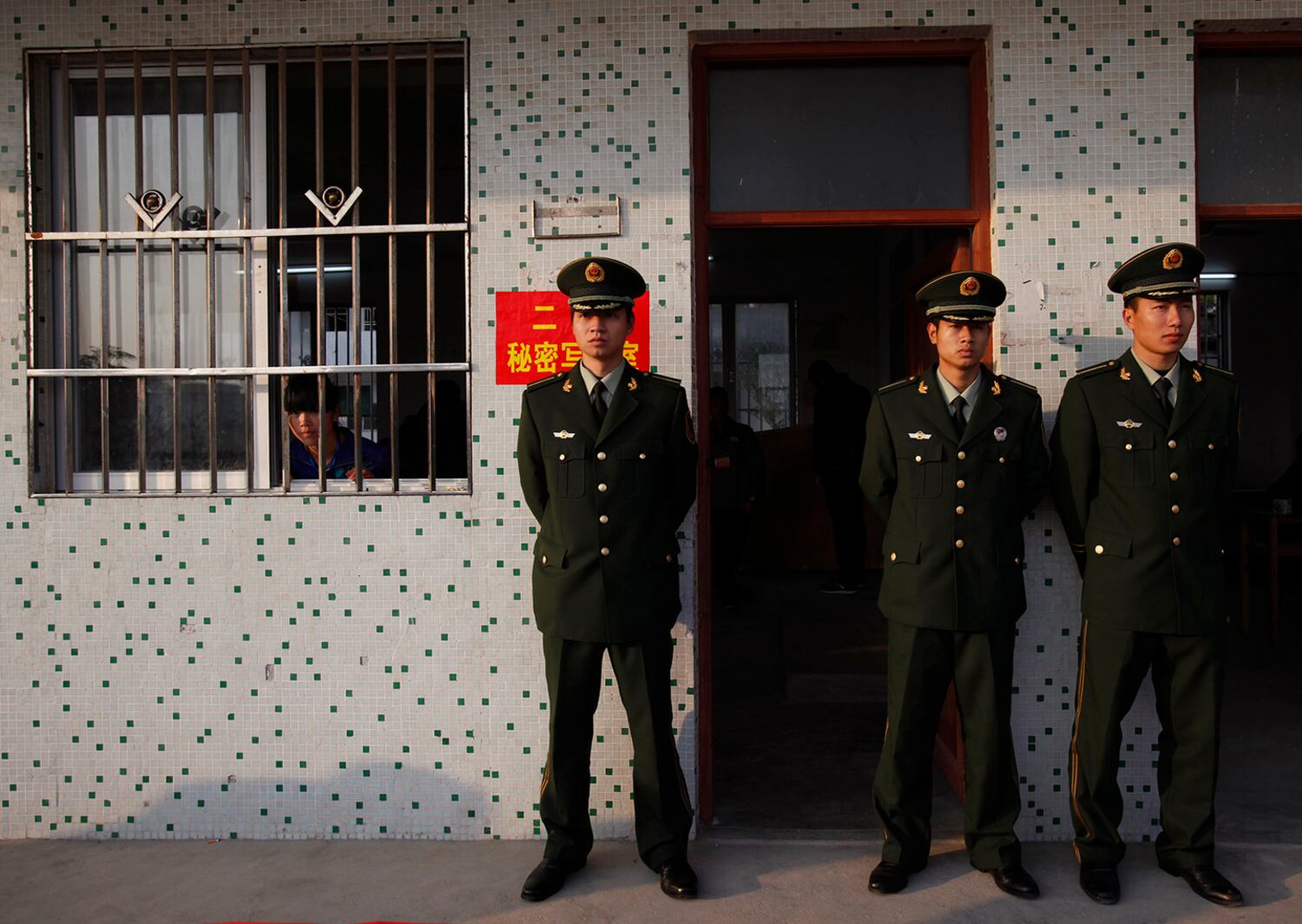 An election worker, left, looks out from a classroom guarded by police officers during vote counting at a school turned into a polling station in Wukan village in Lufeng, Guangdong province, Feb. 1, 2012.
