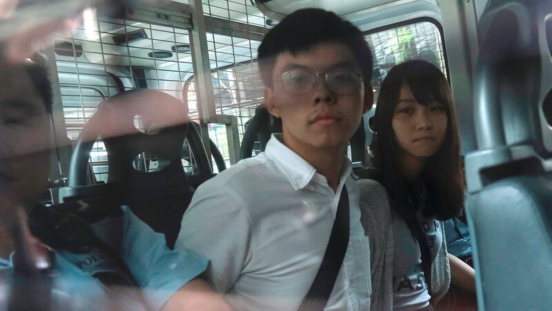 图为,前香港众志秘书长黄之锋、成员周庭被警车押送至法院。(法新社)
