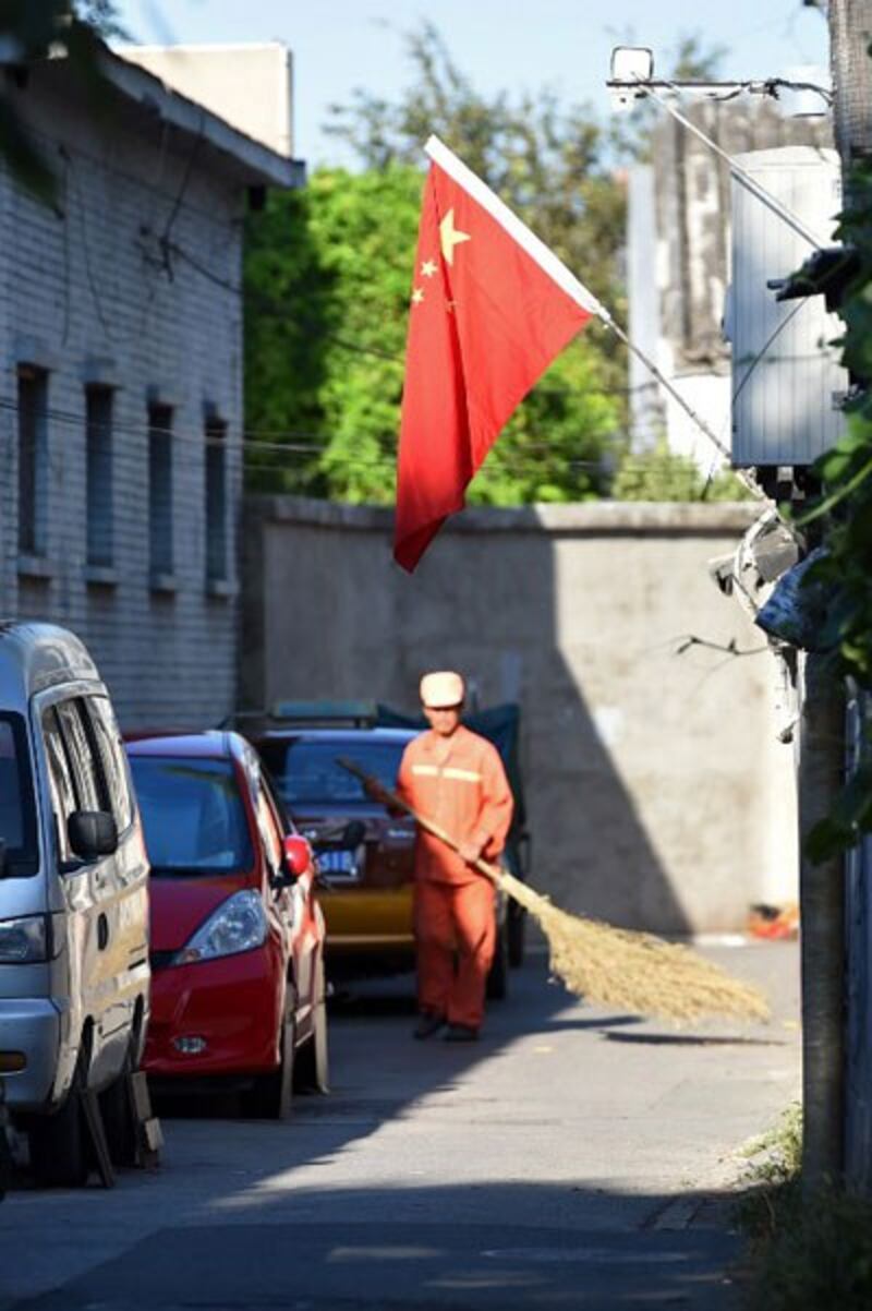 Một công nhân quét đường ở Bắc Kinh dưới lá cờ Trung Quốc trong một con hẻm nhỏ. AFP photo 