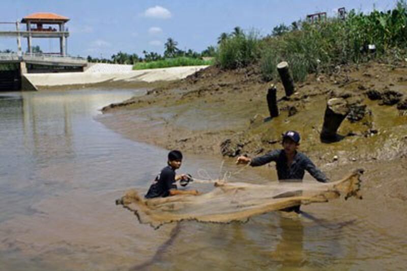Hai người đàn ông lưới cá bên cạnh một đập ngăn mặn trên một con kênh đã gần cạn ở Sóc Trăng hôm 8/3/2016. AFP photo