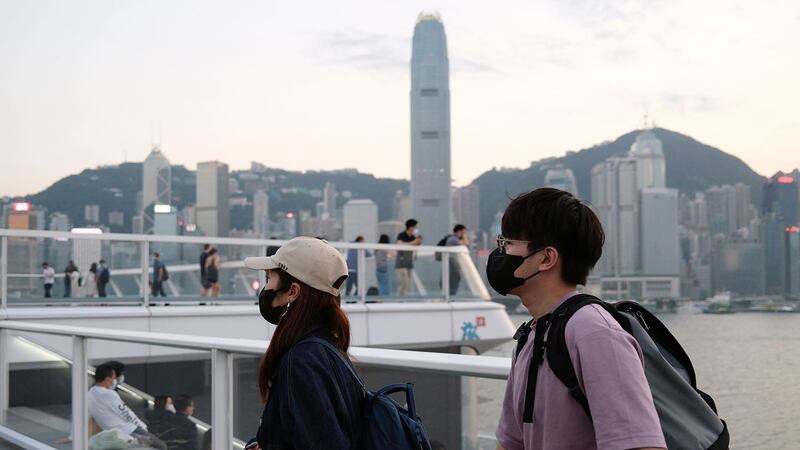 图为，2020年3月23日，戴着防护口罩的人走在香港天际线前。（路透社）