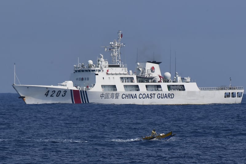 A China Coast Guard ship monitors a Philippine fisherman aboard his wooden boat in the disputed South China Sea,  May 16, 2024.