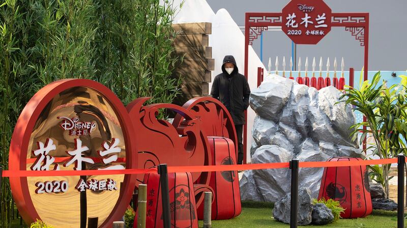 北京的一名男子站在宣传《花木兰》电影的广告牌前。（美联社）