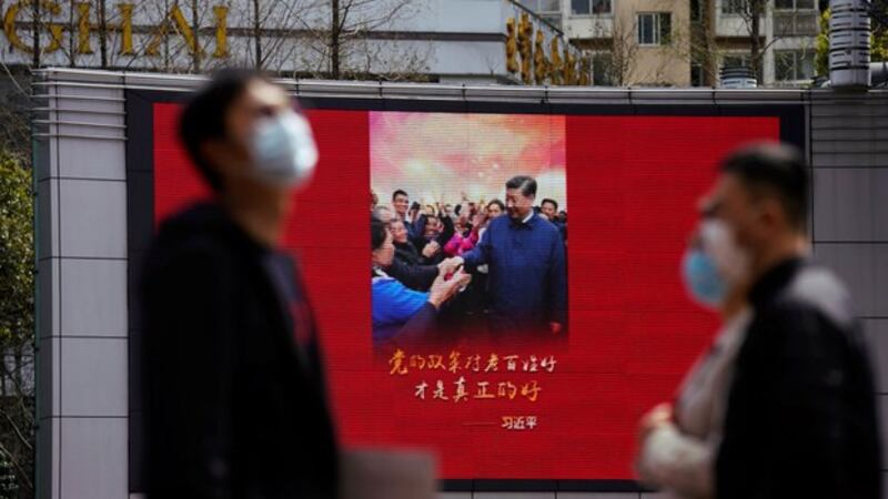 中国国内无症状感染者的频繁出现已引起民众高度恐慌。图为上海戴口罩的行人走过一幅显示中国国家主席习近平图像的屏幕。(路透社)
