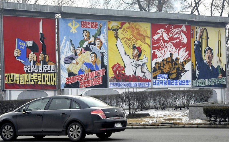 2010년 12월 21일, 북한 평양의 한 도로에서 경제 건설과 군을 찬양하는 선전 간판 옆으로 차량 한 대가 지나가고 있다.
