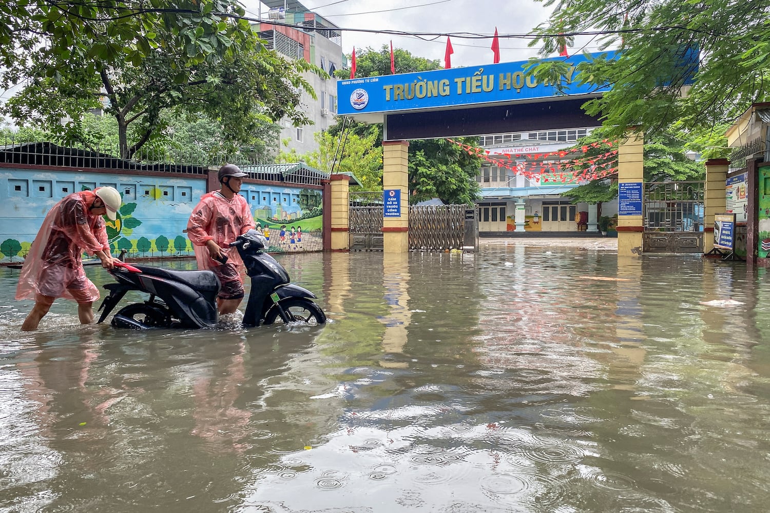 People push a motorcycle as they wade through a flooded street amid heavy downpours from Typhoon Matmo, which stranded vehicles, closed schools, moved classes online, and delayed flights to and from Noi Bai International Airport, in Hanoi, Vietnam, October 7, 2025.