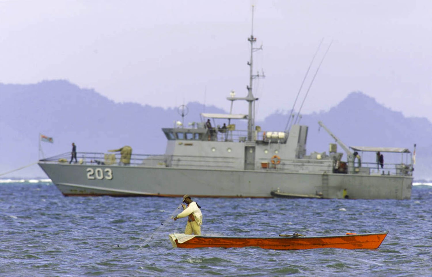 A fisherman pulls in his net as a Fijian naval vessel lies at anchor near the port of Suva May 26, 2000.