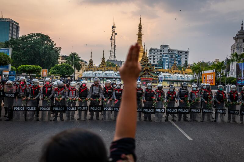 A protester makes a three-finger salute in front of a row of riot police, who are holding roses given to them by protesters, on February 6, 2021 in Yangon, Myanmar.