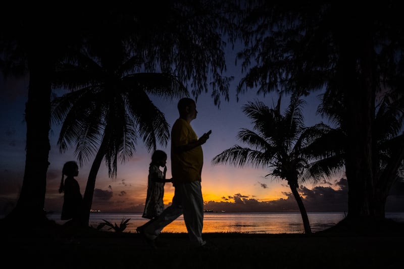 People walk past a beach during sunset in Saipan, Northern Mariana Islands on June 27, 2024.