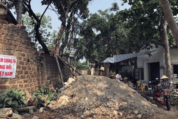 A villager pushes her electric bike on a road partially blocked by rocks, wood and debris amid a showdown between farmers and police at Dong Tam on the outskirts of Vietnam's capital Hanoi, April 20, 2017.