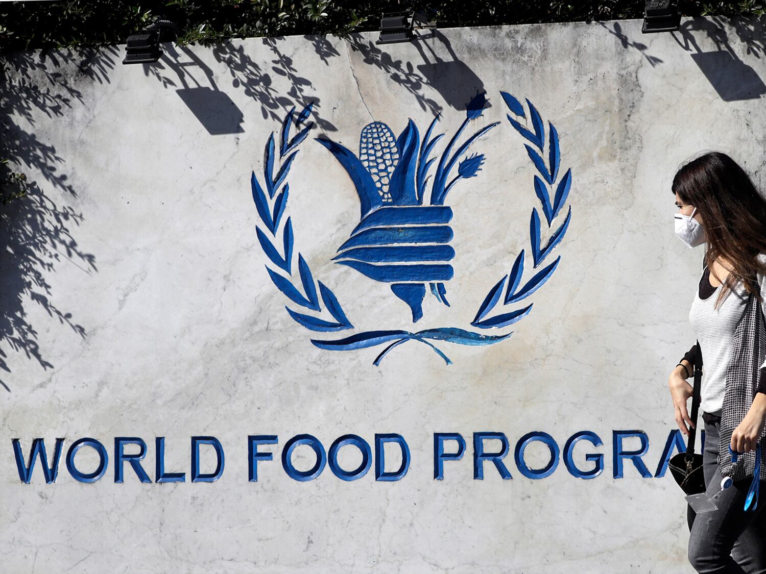 A woman walks past a sign at the entrance of the United Nations World Food Program headquarters in Rome, Oct. 9, 2020.