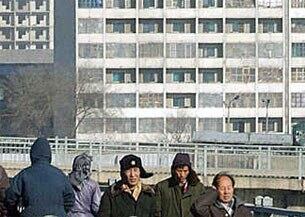 평양거리의 시민들이 매서운바람에 귀를 막고 다리를 건너고 있다. 뒤로보이는 아파트 베란다는 추운날씨를 대비해 비닐로 막아놓았다.