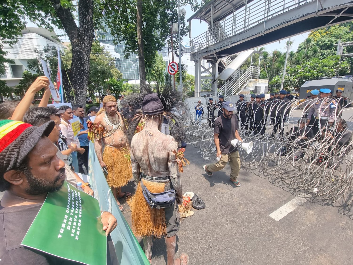 Security personnel watch from behind barbed wire as indigenous Papuans from Merauke in eastern Indonesia protest in Jakarta on Oct. 16, 2024 against plans to convert indigenous and conservation lands into sugar cane plantations and rice fields.