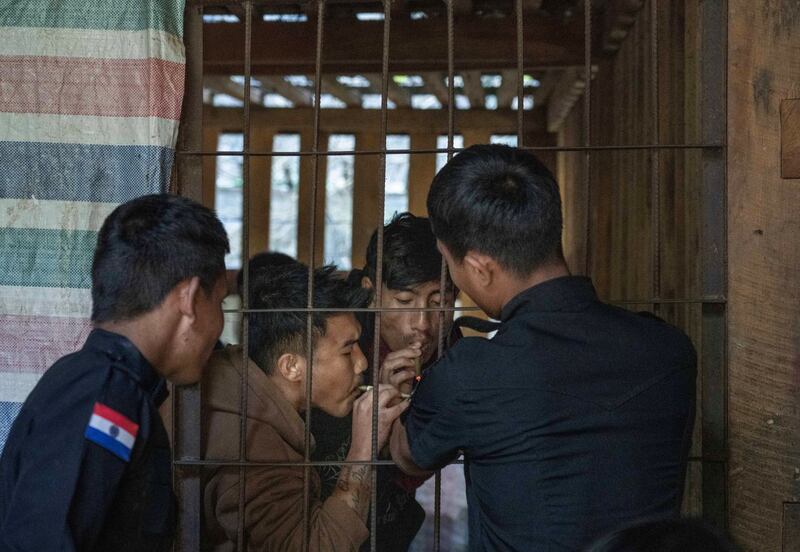 ရှမ်းပြည်နယ်တောင်ပိုင်းရှိ ကရင်နီပြည်ရဲဌာန အမှတ် (၈) စခန်းတွင် ထိန်းသိမ်းထားသူနှစ်ဦးကို တာဝန်ကျရဲအရာရှိတစ်ဦးက ဆေးလိပ်မီးညှိပေးနေသည်ကို ၂၀၂၄ ခုနှစ် နိုဝင်ဘာ ၄ ရက်နေ့က တွေ့ရစဉ်။ (Gemunu Amarasinghe/RFA)