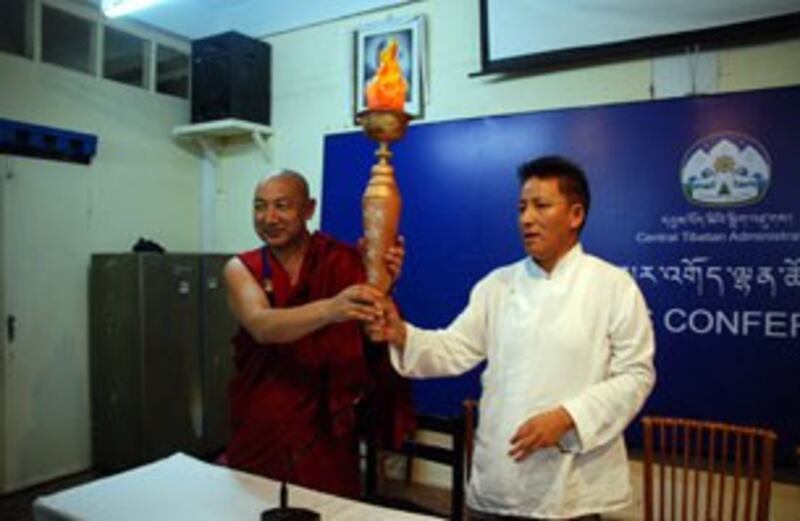图片：议员莫朗塔青（僧）和嘎玛益西手举即将在全球传递的火炬型“西藏油灯”（记者丹珍拍摄）