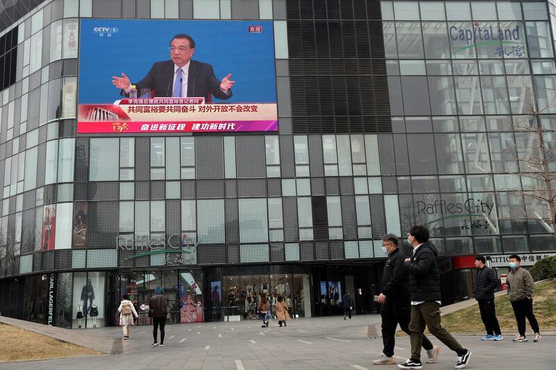 People walk past a giant screen showing a news conference by Chinese Premier Li Keqiang, following the closing session of the National People's Congress (NPC) at the Great Hall of the People in Beijing, March 11, 2022. Credit: Reuters