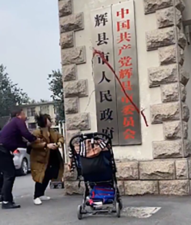 疫苗受害者家长何方美在河南辉县政府牌匾上泼洒红色油漆后被保安带走(QQ截图)