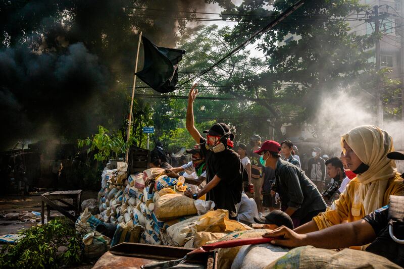 Anti-coup protesters shout slogans towards approaching security forces as smoke rises from burning car tires on March 28, 2021 in Yangon, Myanmar.