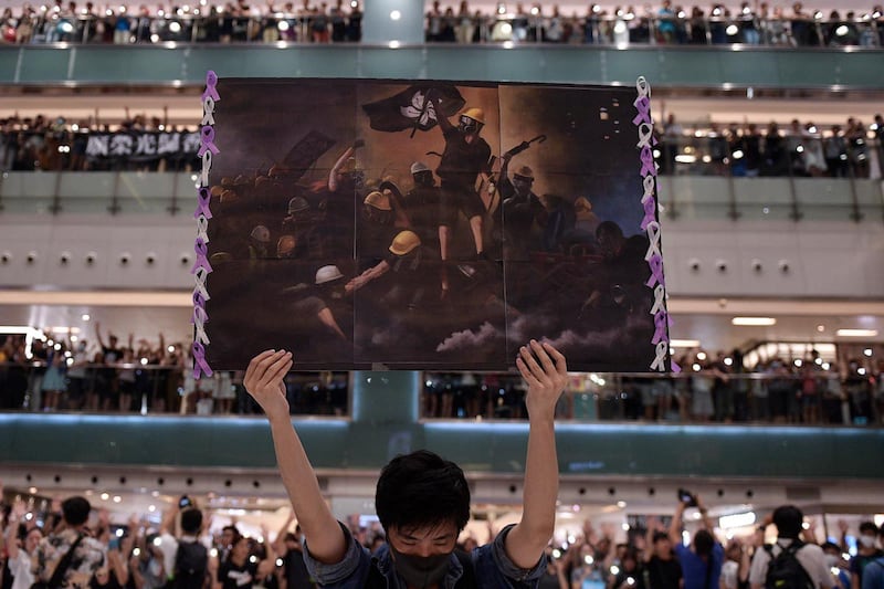香港的大学学生会组织在国安法实施后，正成为北京当局的重点打击目标。图为，2019年9月11日，一位男子在香港沙田高举海報，一旁人们正聚集齐唱抗争歌曲。（攝影／Nicolas Asfouri／AFP）