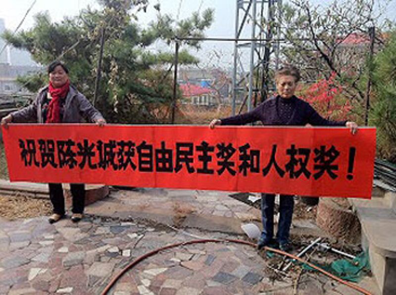 山東臨沂拆遷戶劉國慧、秦玉玲手持他們製作的橫幅，幾經辛苦終把橫額送到陳光福手中。（拆遷戶提供）