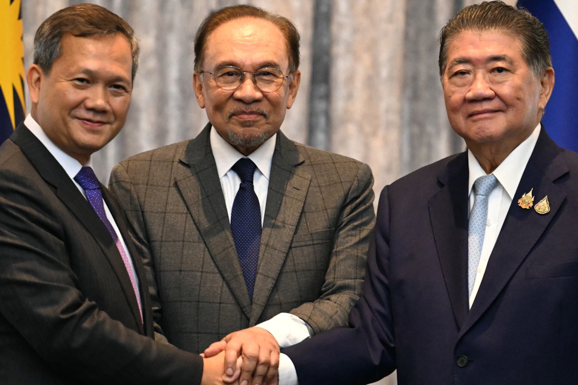 Malaysia's Prime Minister Anwar Ibrahim (C), Cambodia's Prime Minister Hun Manet (L) and Thailand's acting Prime Minister Phumtham Wechayachai (R) pose for photos as they shake hands following a press conference after talks on a possible ceasefire between Thailand and Cambodia in Putrajaya on July 28, 2025.