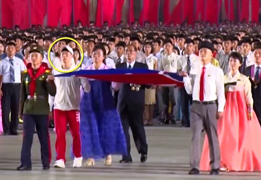 9.9절 행사에서 국기게양 대표 6명 가운데, 탁구 국가대표인 리정식 선수(원 표시)가 체육복을 입고 인공기를 들고 행진하고 있다.