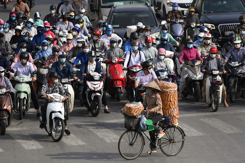 Một người bán bánh mỳ rong đi ngang qua những người điều khiển xe gắn máy đang đứng chờ đèn đỏ. Ảnh chụp tại Hà Nội ngày 2/6/2021.