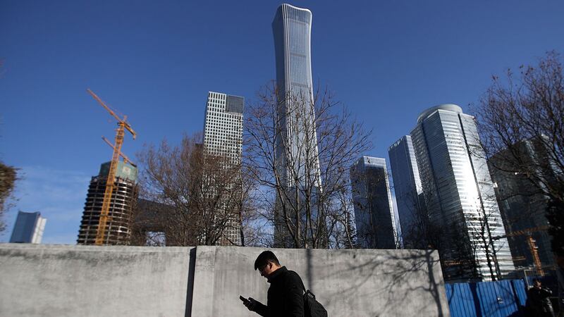 一名男子在北京中央商务区正在建设的摩天大楼旁行走时浏览智能手机。（美联社）