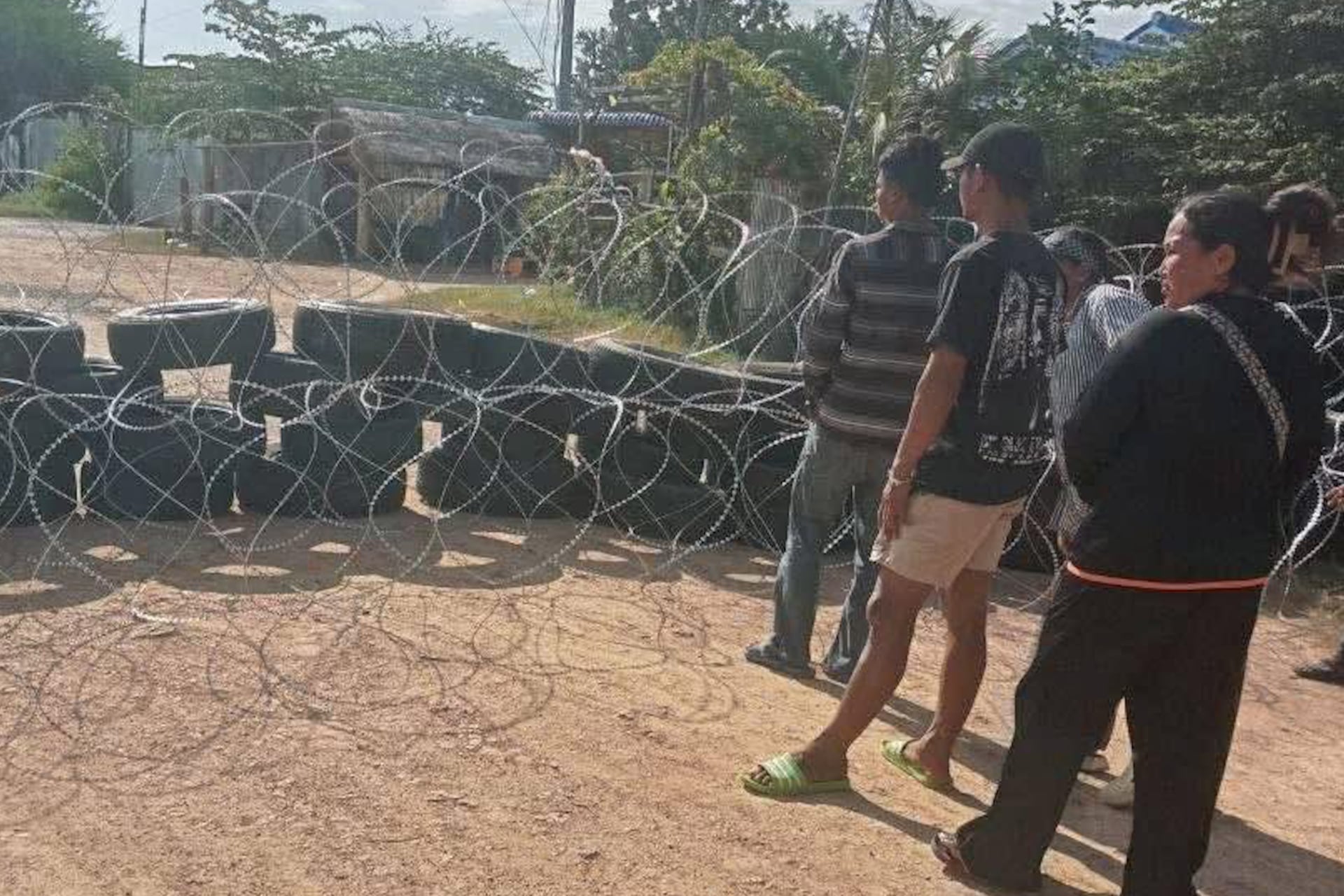 Cambodian residents stand near the barbed wire fences that Thai soldiers have set up to block the entrance to their homes in Ou Beicha-on commune, Ou Chrov district, Banteay Meanchey province, on August 13, 2025.
