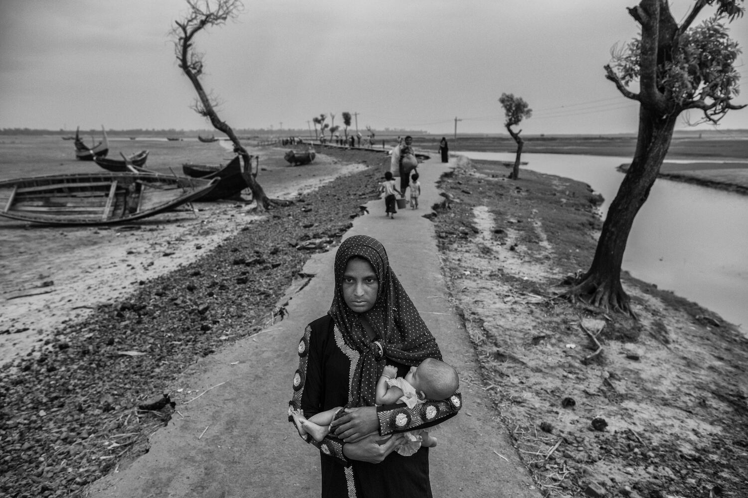 Una refugiada rohingya recién llegada carga a su hijo por una carretera rota después de llegar a Shah Porir Dwip, cerca de Cox's Bazar, Bangladesh, el 29 de octubre de 2017. (Kevin Frayer/Getty Images)