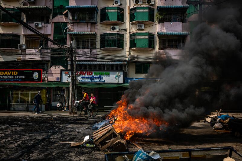 Residents ride a bicycle past tires set alight by anti-coup protesters at a blockade on March 28, 2021 in Yangon, Myanmar.