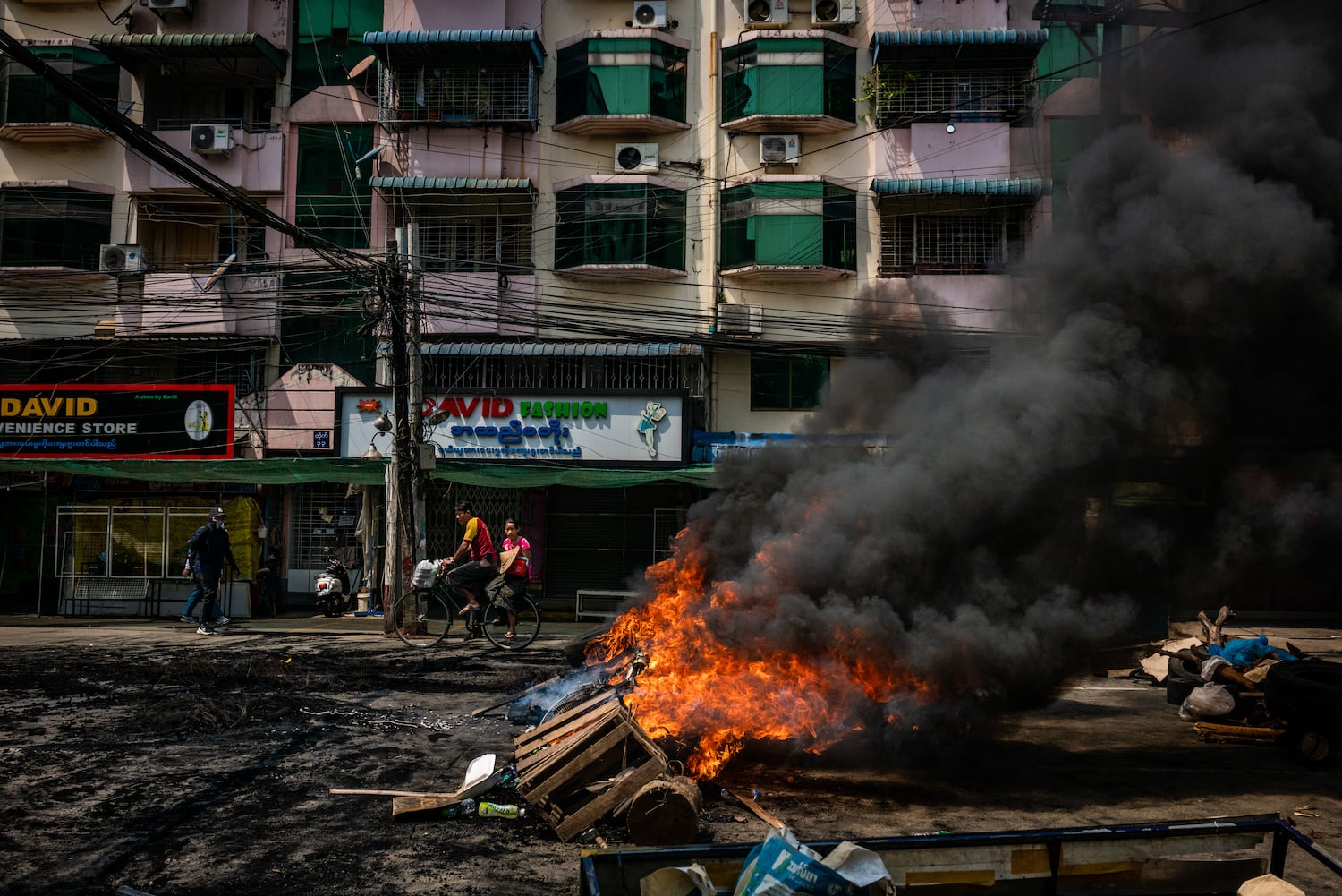 Residents ride a bicycle past tires set alight by anti-coup protesters at a blockade on March 28, 2021 in Yangon, Myanmar. 
