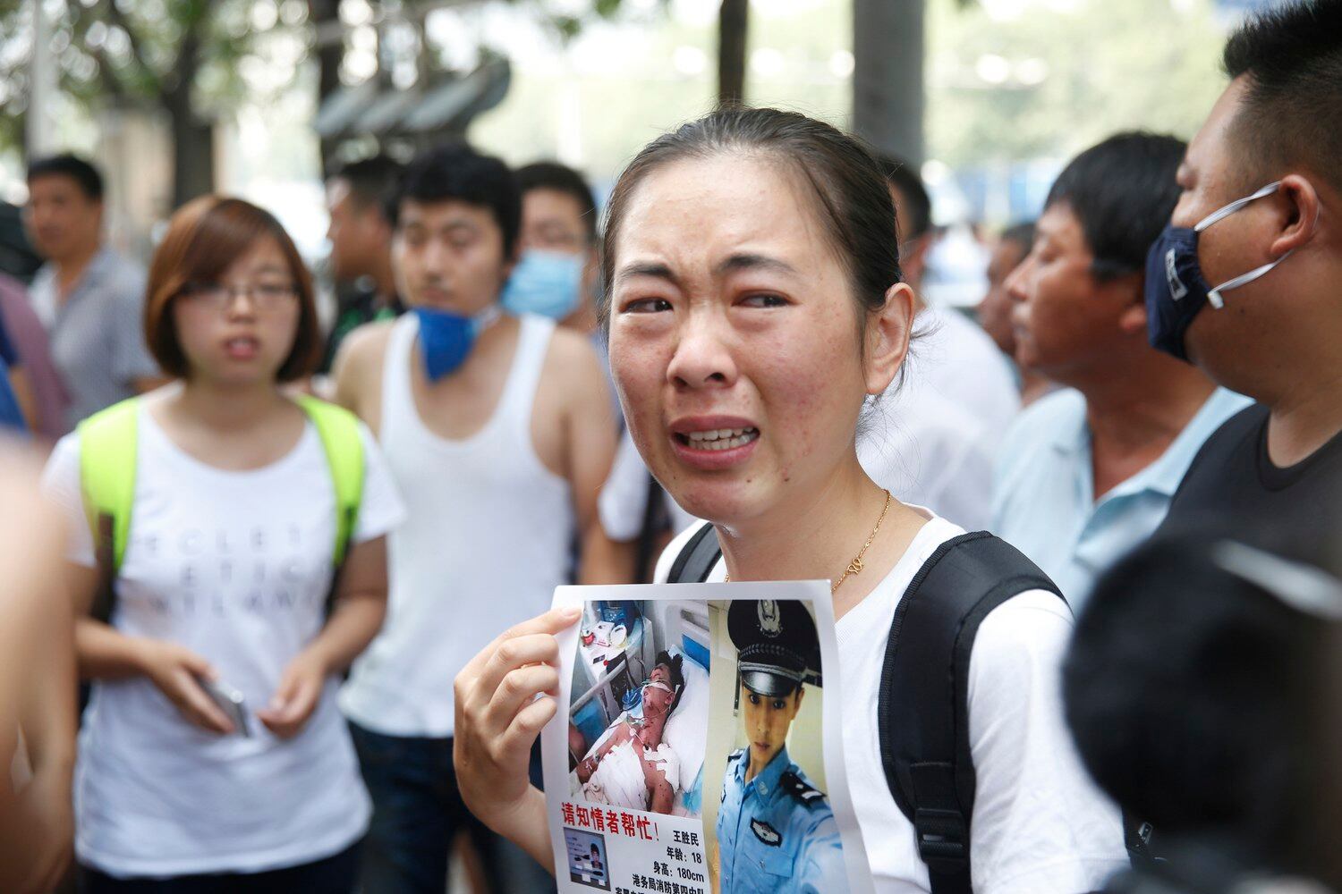 图片:2015年8月16日,一名失踪消防员的家属手举亲人照片出现在天津爆炸事故新闻发布会场外。(AFP PHOTO)