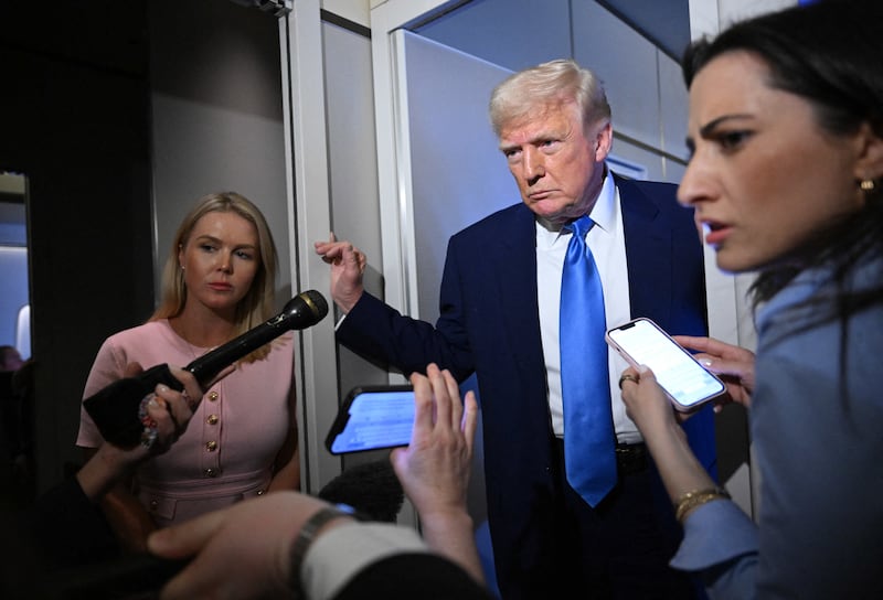 White House Press Secretary Karoline Leavitt listens (L) as U.S. President Donald Trump speaks to reporters while in flight on Air Force One, en route to Joint Base Andrews on April 6, 2025.