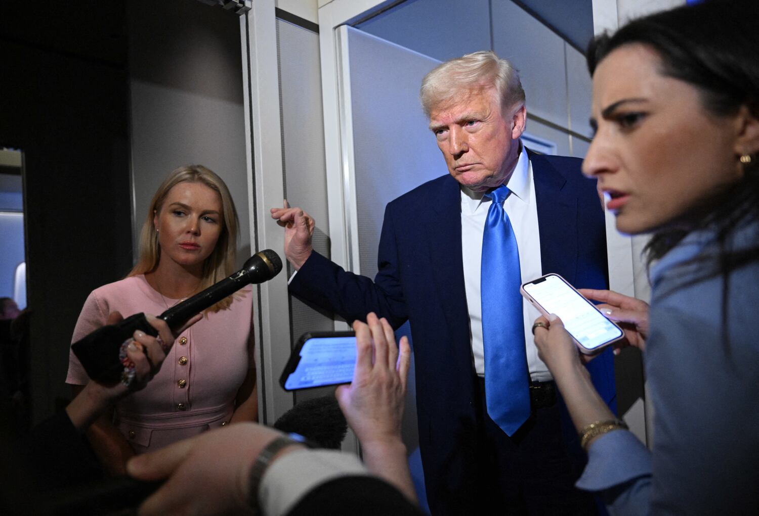 White House Press Secretary Karoline Leavitt listens (L) as U.S. President Donald Trump speaks to reporters while in flight on Air Force One, en route to Joint Base Andrews on April 6, 2025.