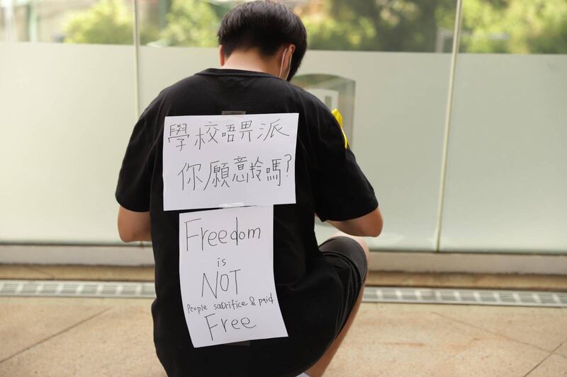 身穿黑色T-shirt的戴嘉平除了掛上黃絲帶，亦在背面寫上一張「學校唔畀我哋派，你哋願意拎嗎？」「Freedom is NOT Free. People sacrifice & paid」（自由不是免費，是人們犧性和付出的）白紙。（讀者提供相片）