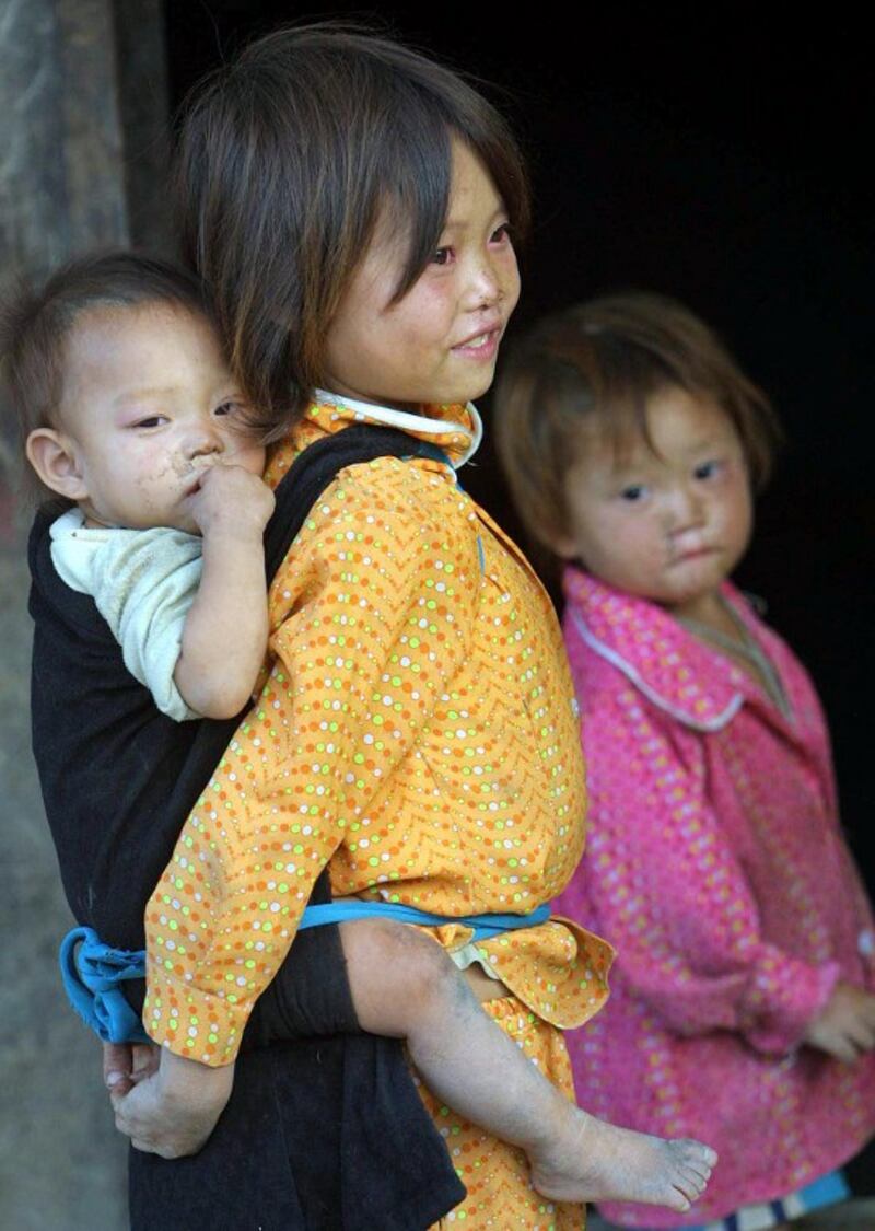 Một bé gái H'mông cõng em trai và trông em gái ở nhà. Ảnh ngày 9 tháng 10 năm 2002.