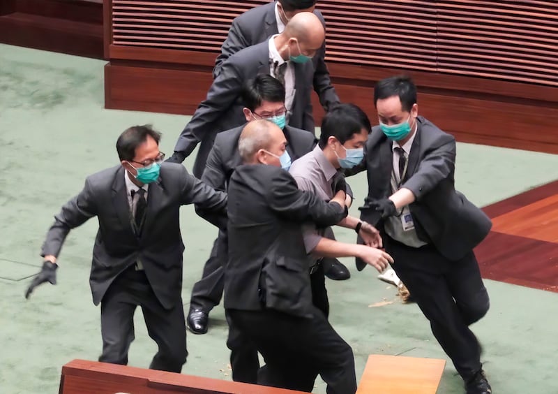 In this May 28, 2020, file photo Pro-democracy lawmaker Ted Hui, center, struggles with security personnel at the main chamber of the Legislative Council during the second day of debate on a bill that would criminalize insulting or abusing the Chinese anthem in Hong Kong.