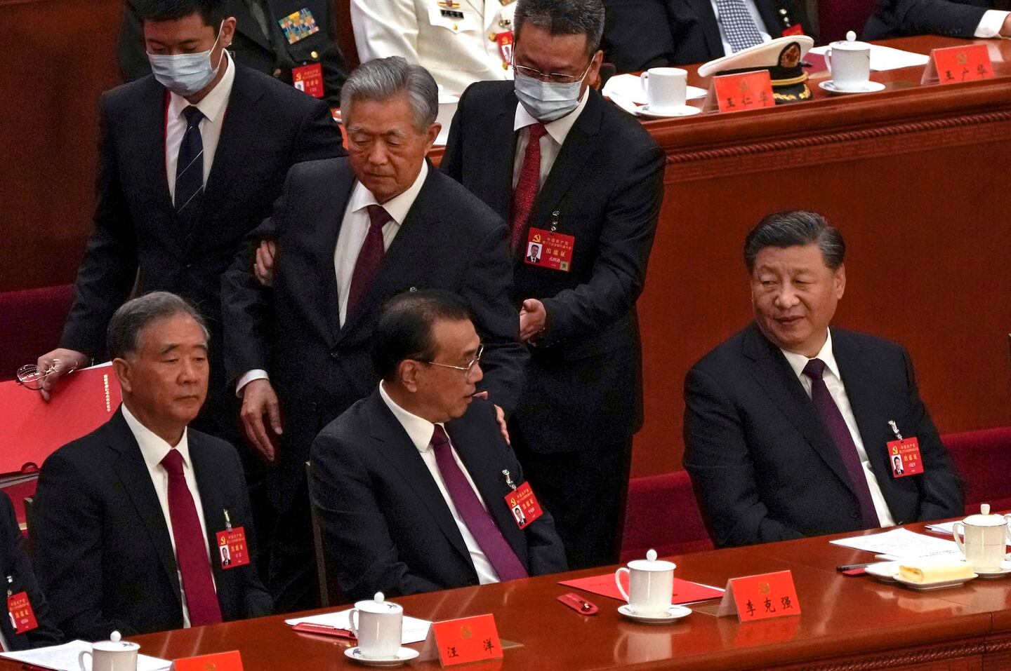 Chinese President Xi Jinping, right, looks on as former Chinese President Hu Jintao, standing at center, touches the shoulder of Premier Li Keqiang, center, as he is assisted to leave the hall during the closing ceremony of the 20th National Congress of China's ruling Communist Party at the Great Ha