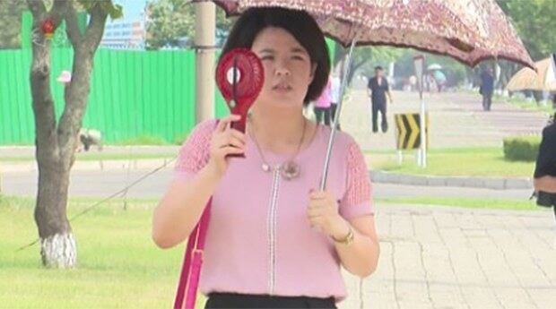 조선중앙TV가 2일 공개한 영상 속에서 한 주민이 양산을 쓰고 손 선풍기를 사용하며 더위를 식히고 있다.