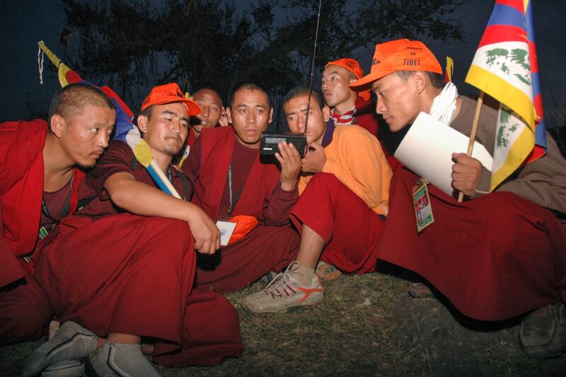 Tibetan monks listen to a Radio Free Asia broadcast as they march to protest China's hosting of the Olympic Games in Takipur, outside Dharamsala, India, March 11, 2008.
