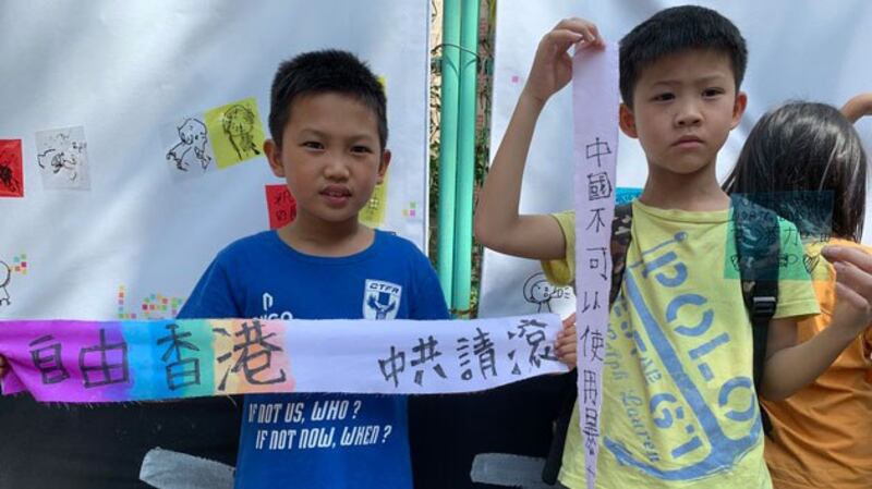 两位亲子团幼童拿着手写的布条准备系于儿童连侬墙。(记者 黄春梅摄)