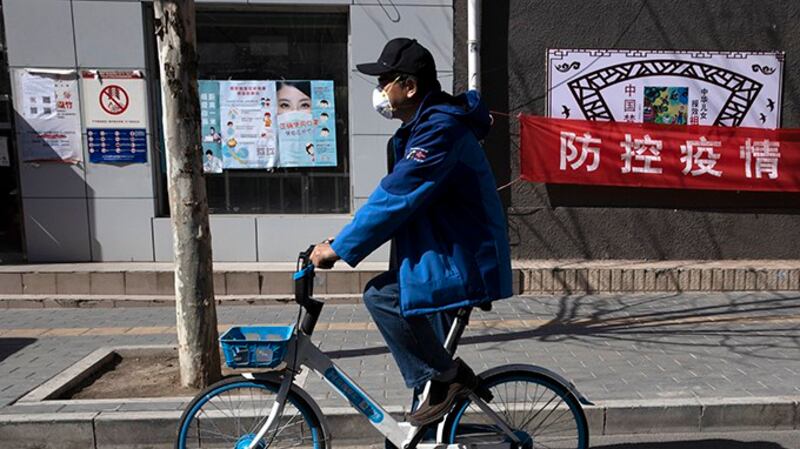 2020年3月12日，北京一名男子骑车经过“防控疫情”宣传口号。（美联社）
