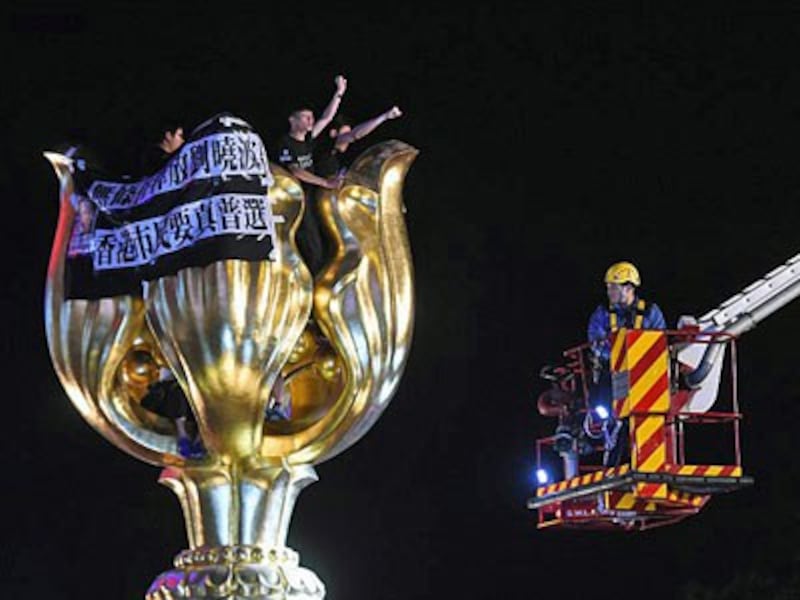 Pro-democracy demonstrators chant slogans as a fire engine crewmember attempts to remove them from the Golden Bauhinia statue in Hong Kong, June 28, 2017.