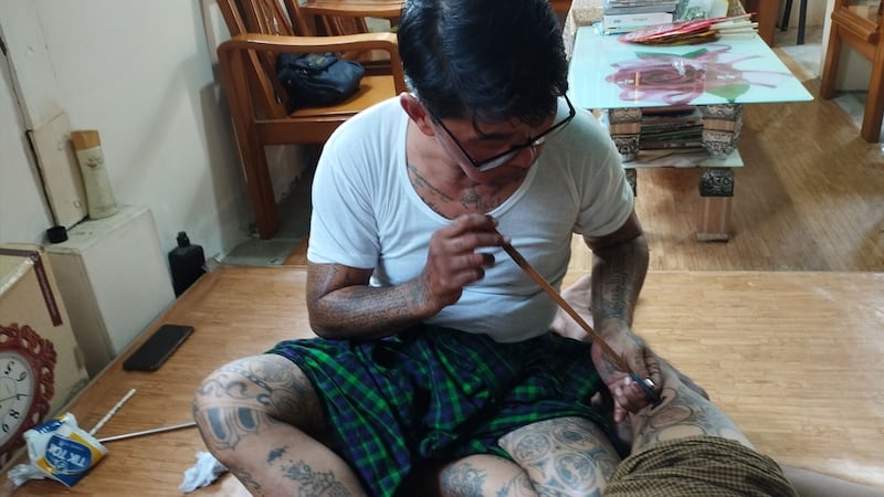 မန္တလေးမြို့မှ မြန်မာ့ရိုးရာဆေးမင်ကြောင်ဆရာ ဦးသက်နိုင် ဆေးမင်ကြောင်ထိုးပေးနေသည်ကို ၂၀၂၃ ခုနှစ်၊ ဇူလိုင်လ ၁၈ ရက်နေ့က တွေ့ရစဉ်။ (Photo: RFA)