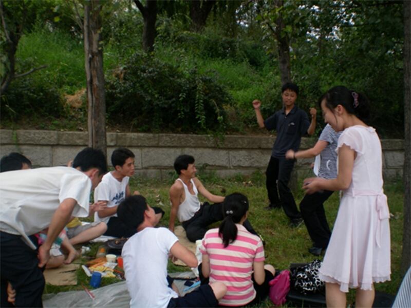 휴일에 풀밭 나무그늘 아래서 친구들과 춤을 추며 즐거운 한 때를 보내고 있는 북한 젊은이들(2011년 8월). 