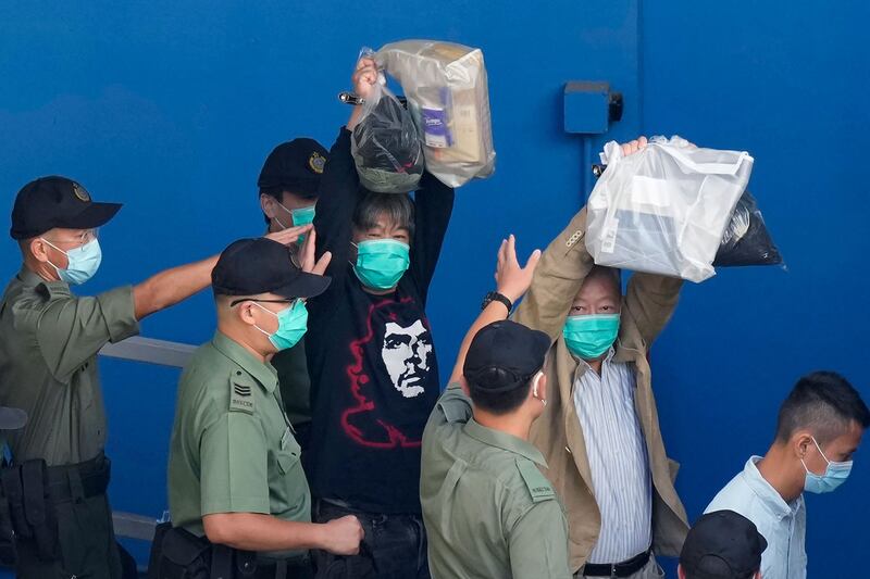 2021年5月28日,香港民主运动人士梁国雄(左)被称为“长发”,和李卓人在惩教人员的陪同下举手,到监狱看守车上。 (美联社)