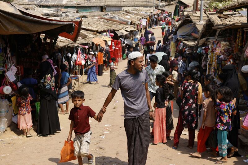 A Rohingya refugee man walks with a child in a market, at the Rohingya refugee camp in Cox's Bazar, Bangladesh, March 15, 2025. REUTERS/Mohammad Ponir Hossain